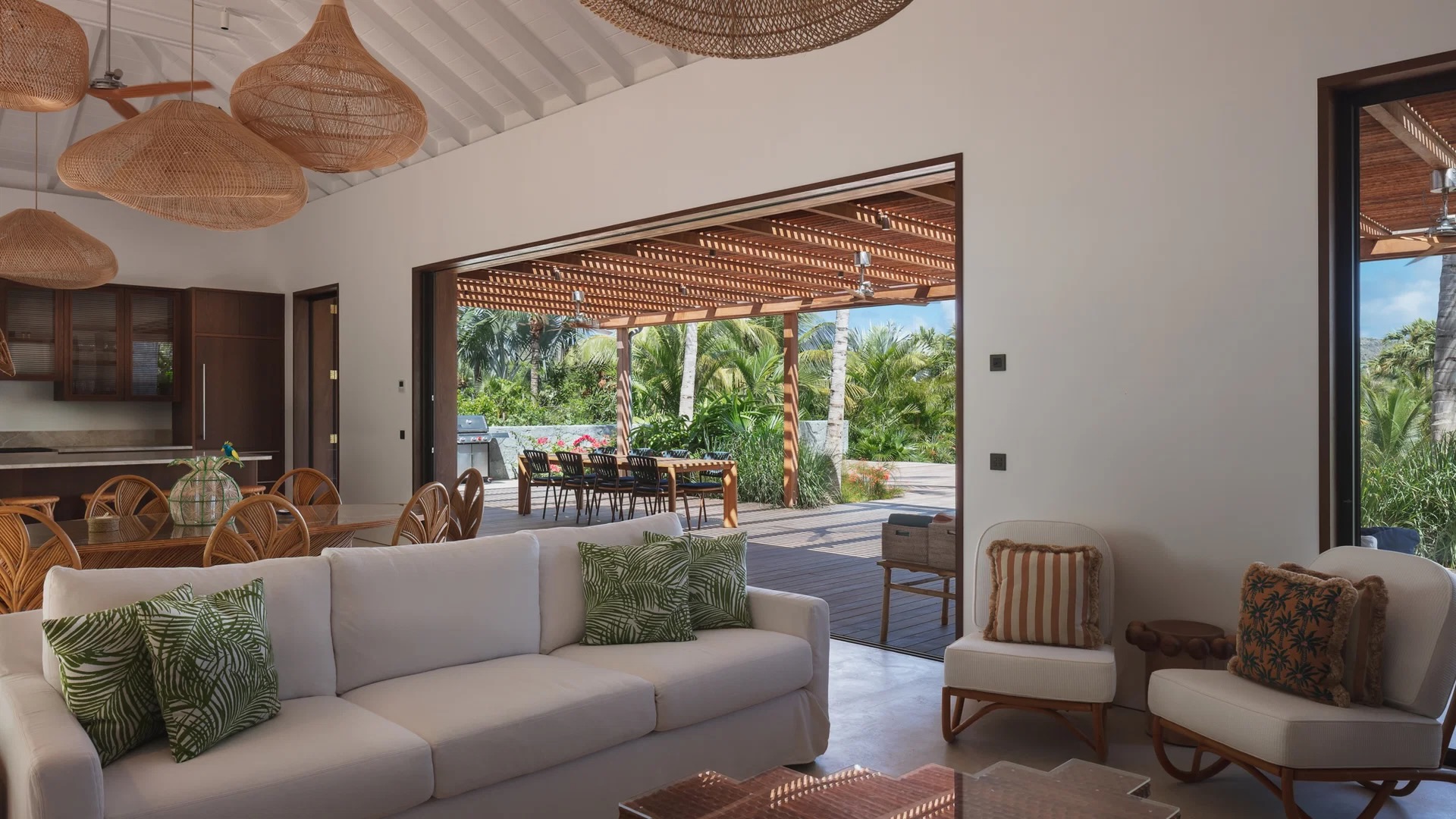 Luxurious living area features a white sofa, elegant decor, and opens to a scenic outdoor dining space surrounded by greenery.