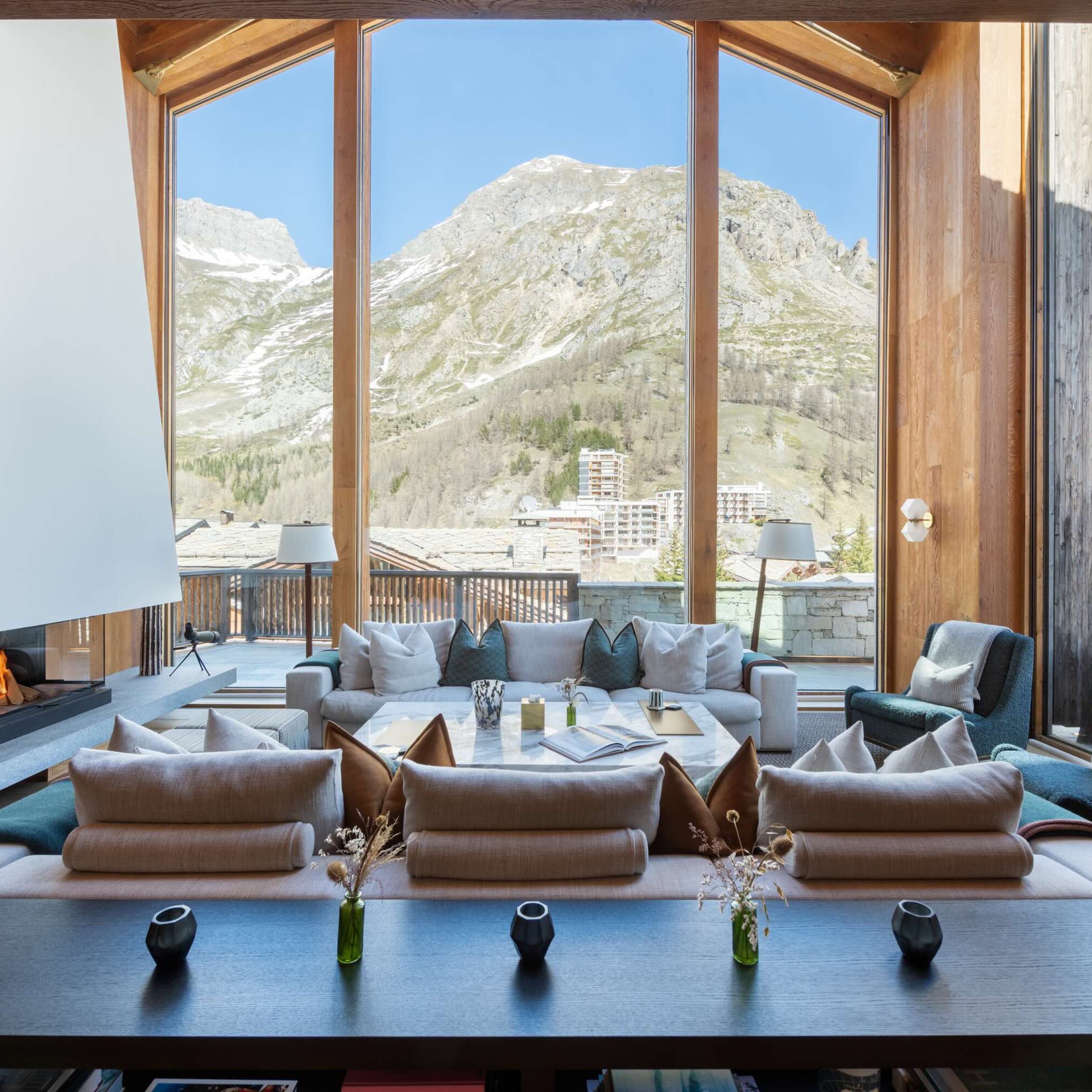 Luxurious living area with panoramic mountain views, a modern fireplace, and stylish furnishings in a chalet setting.