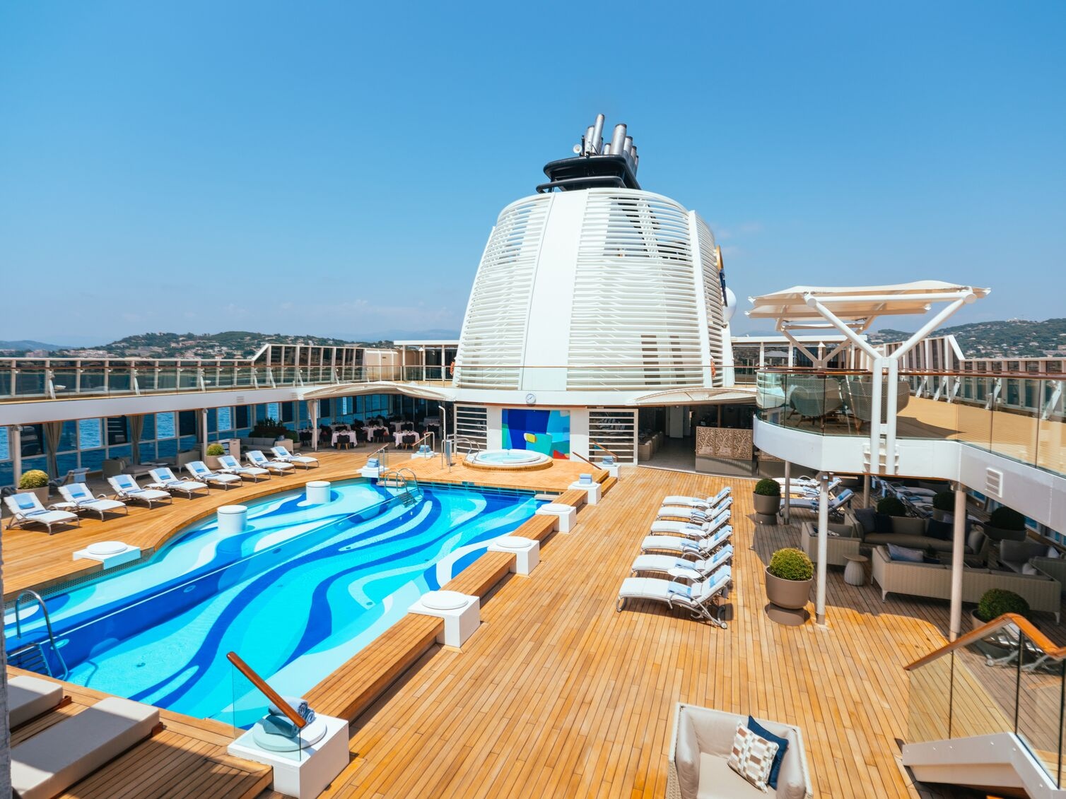 Luxury pool deck with a swirling blue pool, lounge chairs, and panoramic ocean views on the private luxury ship.